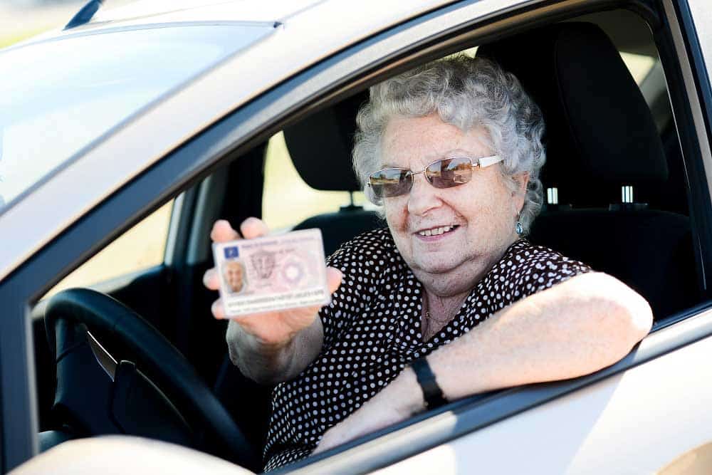 happy cheerful elderly senior woman driving her car and showing her drivers license